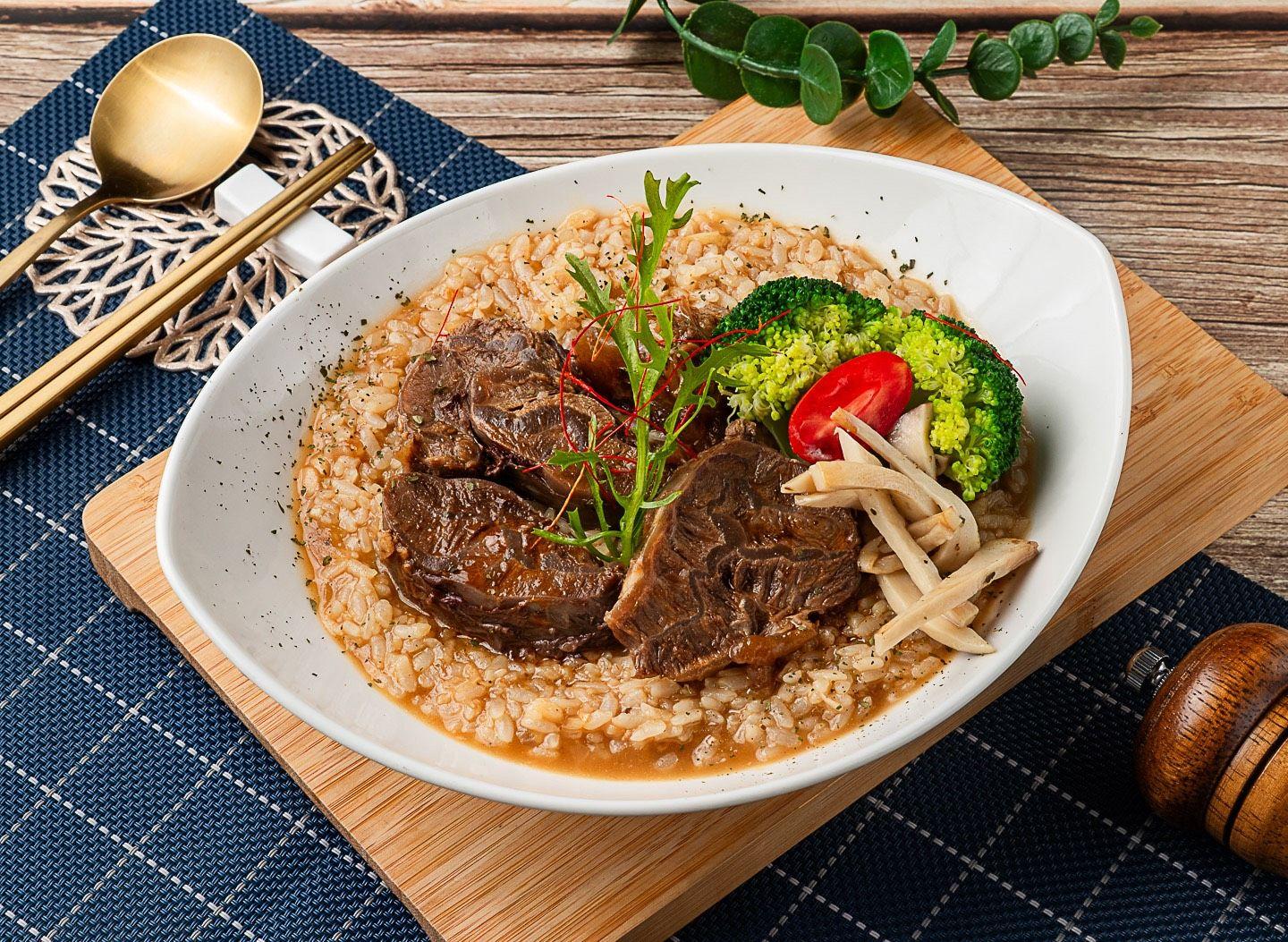 燉飯上鋪著燉牛肉塊、綠花椰與蕈菇，點綴小番茄