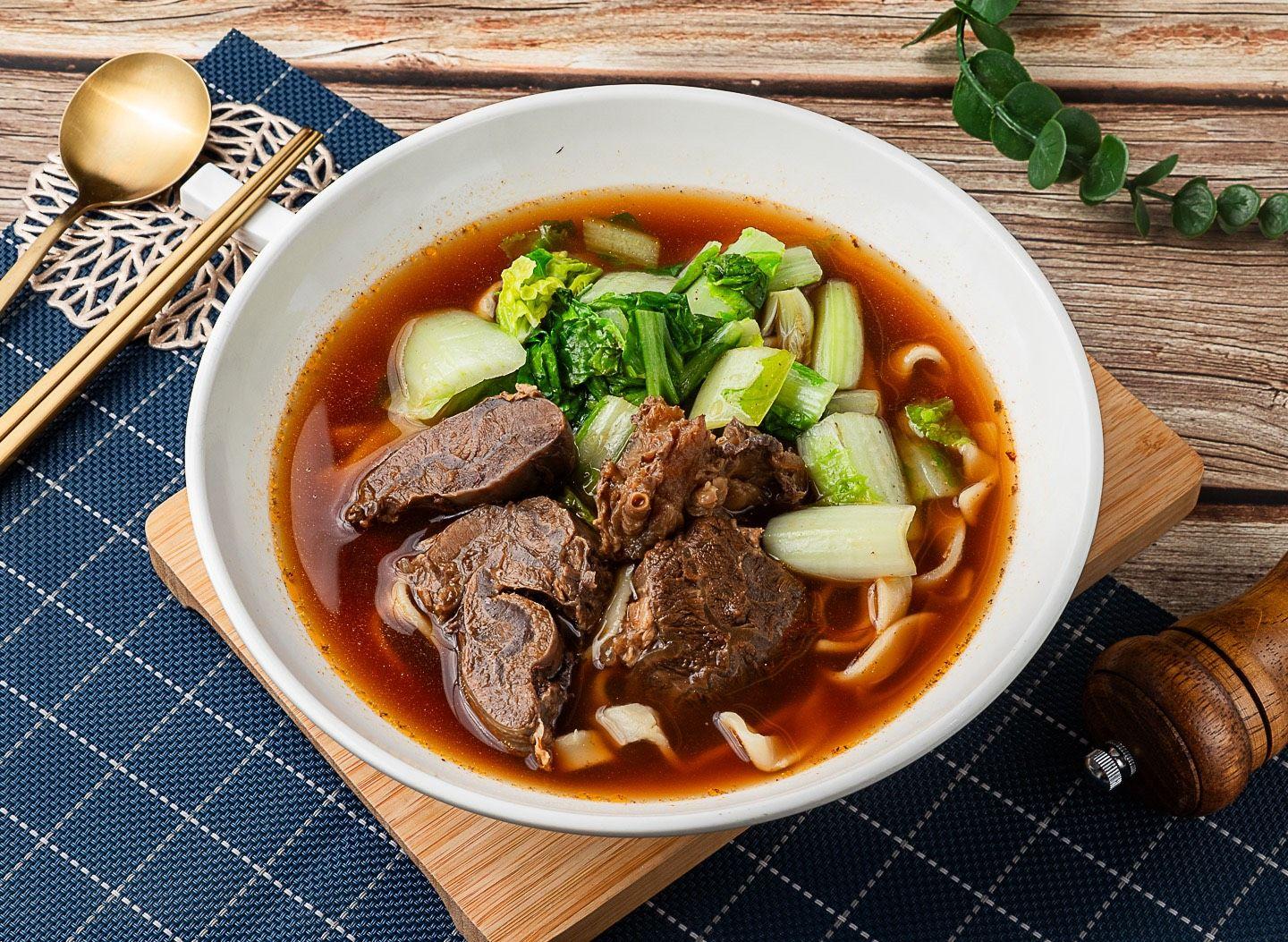 白瓷碗裝的果香牛肉麵，紅褐湯頭裡有大塊牛肉、青江菜與小黃瓜