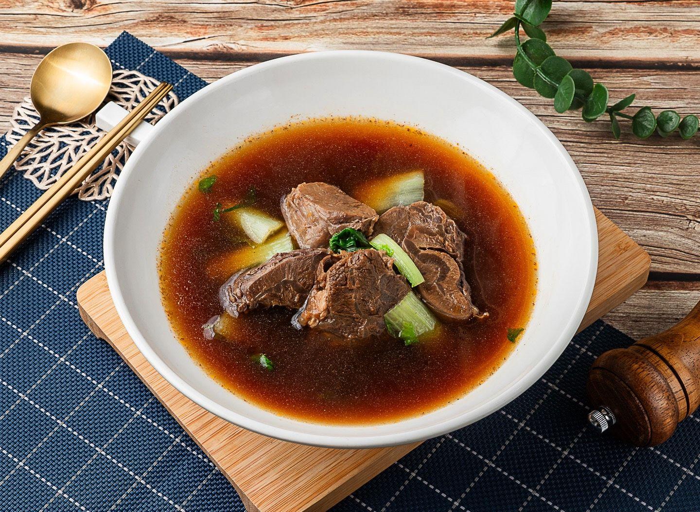 白瓷碗裝的清澈深褐牛肉湯，湯裡有牛肉塊與小黃瓜
